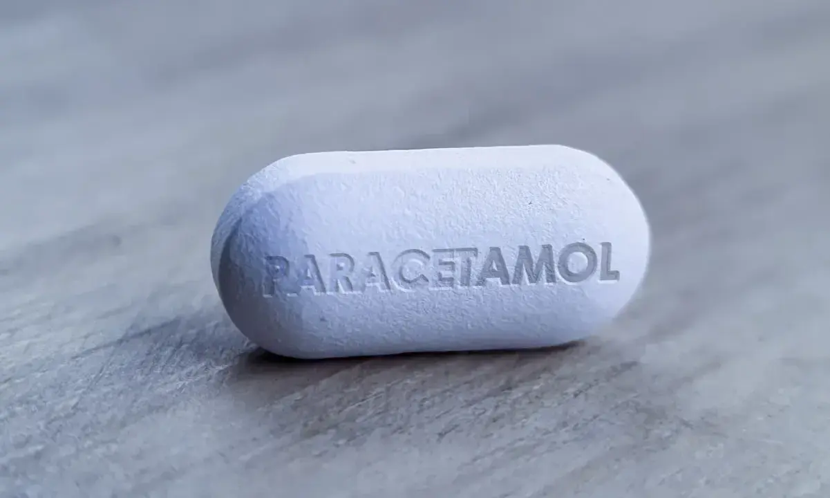 Biała tabletka z napisem "PARACETAMOL" na szarym tle. Dylemat: apap czy paracetamol?