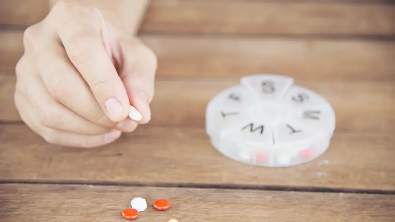 Dłoń trzyma tabletkę. Obok leżą inne pigułki i pojemnik na leki. Captopril 12,5 mg jak długo działa?