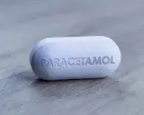Biała tabletka z napisem "PARACETAMOL" na szarym tle. Dylemat: apap czy paracetamol?