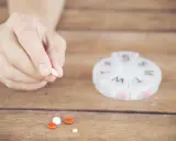 Dłoń trzyma tabletkę. Obok leżą inne pigułki i pojemnik na leki. Captopril 12,5 mg jak długo działa?