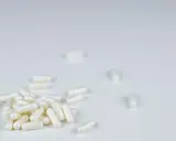 Białe kapsułki leżą na białym tle. To suplementy, które mogą pomóc w walce z bólem, podobnie jak anapran na co jest.
