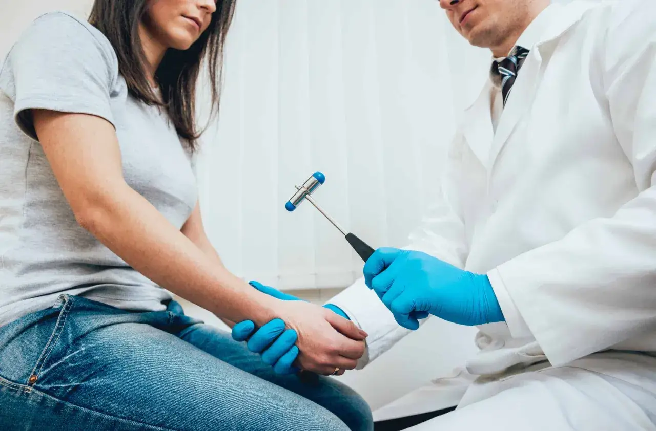 Lekarz w niebieskich rękawiczkach bada odruch kolanowy młoteczkiem neurologicznym u pacjentki.